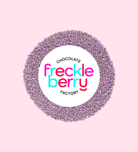 A single purple milk freckle candy, 8cm in diameter, against a pink background.