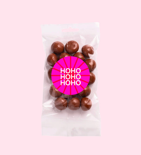 A clear plastic packaging containing milk chocolate coated raspberries with a red Christmas themed label that reads 'Merry Christmas'.