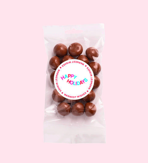 A clear plastic packaging containing milk chocolate coated raspberries with a red Christmas themed label that reads 'Merry Christmas'.