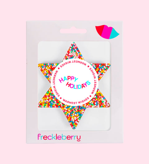A packaged chocolate star shaped with 'Happy Holidays' text and colourful sprinkles design, branded 'freckleberry'.