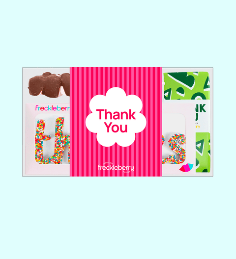 A thank you gift box containing various chocolate treats including a milk chocolate message block, fun rocky road, milk speckles grab bag, mallow pop, and a thanks word. The box is on a white surface with a 'THANK YOU' card beside it.