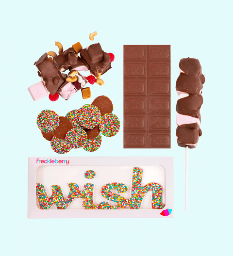 A variety of chocolate treats including a milk chocolate message block, milk rocky road, a milk freckle grab bag, a mallow pop, and a freckle word wish arranged on a white background.