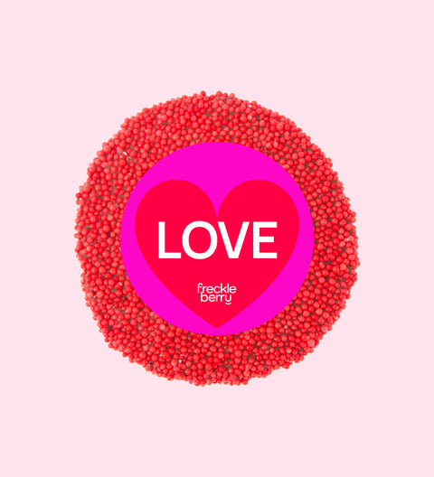 A colorful chocolate freckle with 'LOVE' text and the brand 'freckle berry' written on top, surrounded by multicolored sprinkles.