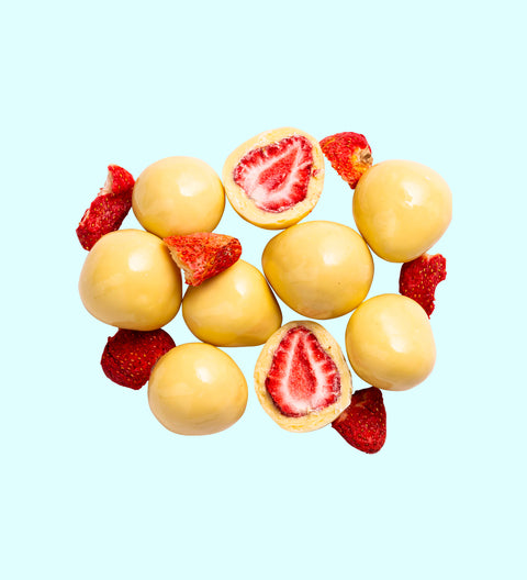 A collection of white chocolate coated freeze-dried strawberries arranged on a white background, with a few strawberries cut in half to show the interior.