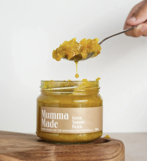 Jar of 'Mumma Made' green tomato pickle with a spoonful being lifted, on a wooden board.