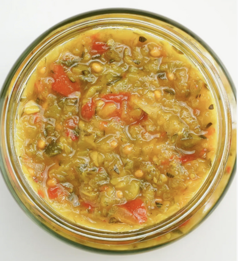 Jar of green zucchini relish with vegetables on a white background