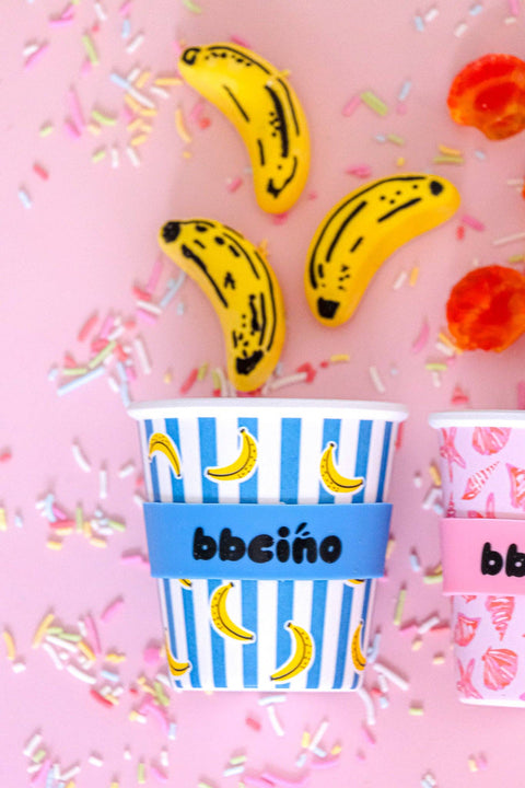 Two novelty bachelorette party cups decorated with banana prints and ice cream cone motifs, complete with matching banana-shaped straws, arranged on a pink background with sprinkles and gummy candies.