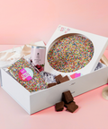 Gift hamper set with colorful sprinkles, chocolate, and a can on a pink background