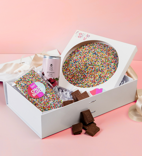 Gift hamper set with colorful sprinkles, chocolate, and a can on a pink background