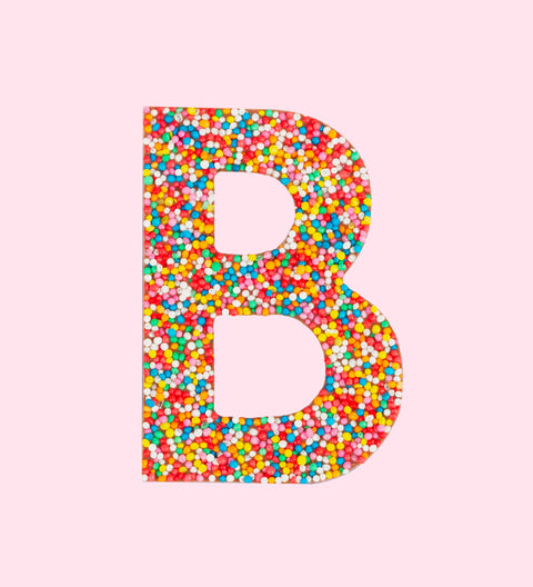 A milk chocolate letter 'B' covered with multicolored sprinkles on a white background