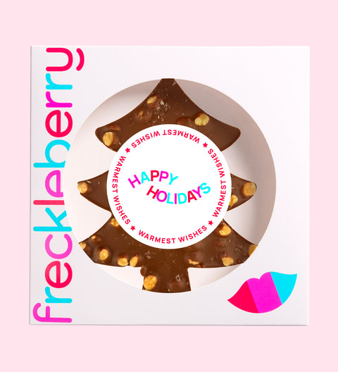 A festive Belgian milk chocolate tree loaded with roasted hazelnuts, gooey caramel, and a sprinkle of sea salt with "Happy Holidays" label/design. 