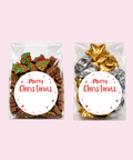 Two clear gift bags filled with holiday treats on a pale pink background. The left bag contains assorted chocolate pieces with red and green sprinkles, and the right bag contains foil-wrapped chocolates in gold and silver.