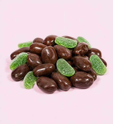 Chocolate-covered almonds with green candy pieces on a pink background