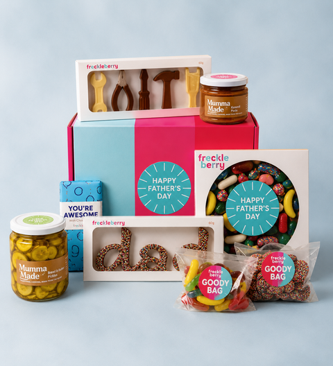 A Father's Day gift set from Freckle Berry and Mamma Made, featuring a pastel blue and pink box filled with chocolate molds, a jar of Mamma Made pickles, a blue box, a candy card, and two 'Good Bag' candy bags on a light blue background.