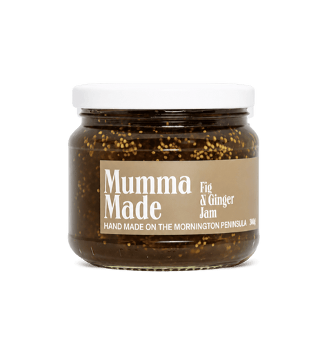 A jar of Mumma Made Fig & Ginger Jam on a solid green background. The product is in a clear glass jar showing the dark jam and visible figs, with a white lid and a beige label.