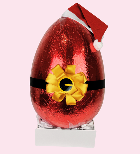 Red chocolate egg with a yellow bow and Santa hat on a white base against a pink background