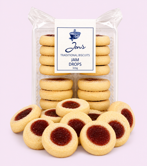 A package of Jen's Traditional Biscuits Jam Drops, with several round golden-brown biscuits arranged in front of the clear plastic bag. Each biscuit has a deep red jam filling in the center, set against a solid pale pink background.