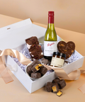 Gift box with wine, chocolate rocky road and honeycomb, candles, and a bottle of wine on a beige background