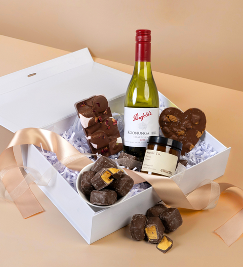 Gift box with wine, chocolate rocky road and honeycomb, candles, and a bottle of wine on a beige background