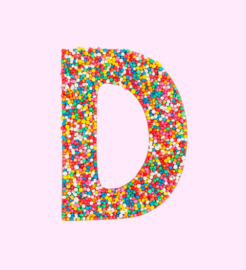 A milk chocolate letter 'D' covered with multicolored sprinkles.