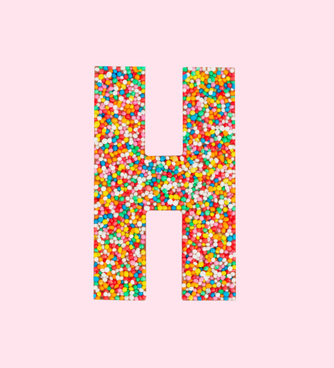 Belgian milk chocolate letter 'H' covered with multicolored sprinkles on a white background