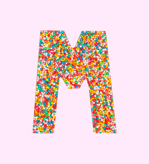 Belgian milk chocolate letter 'M' covered with multicolored sprinkles on a white background