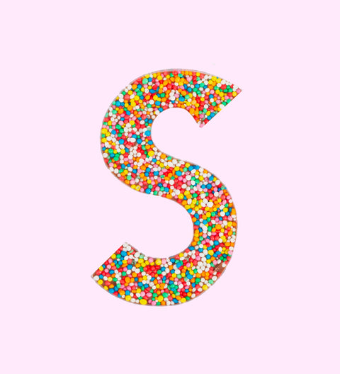 Belgian milk chocolate letter 'S' covered with multicolored sprinkles on a white background