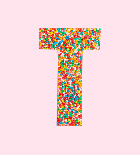 Belgian milk chocolate letter 'T' covered with multicolored sprinkles on top, isolated on a white background.