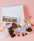 Gift box with chocolate letters, a bottle of champagne, and candies on a pink background