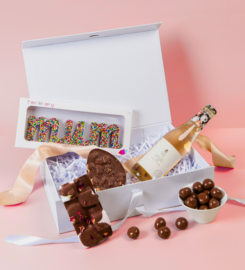 Gift box with chocolate letters, a bottle of champagne, and candies on a pink background