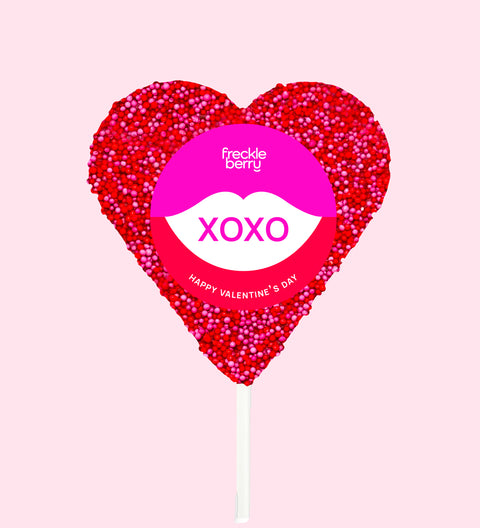 Heart-shaped lollipop with 'Freckle Berry' branding on a pink background