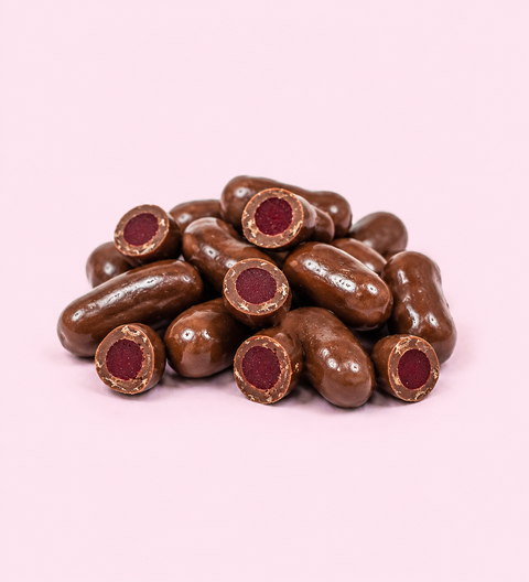 Chocolate-covered candies with red centers on a pink background. Milk chocolate raspberry bullets