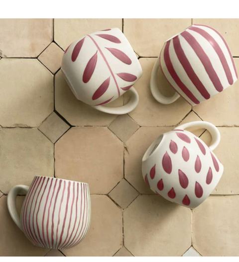Four ceramic mugs with red patterns on a beige tiled floor