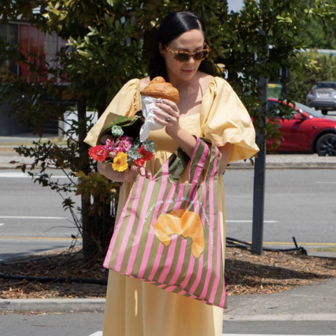 Woman in yellow dress holding a striped bag with a bow, flowers, and a pastry outdoors.
