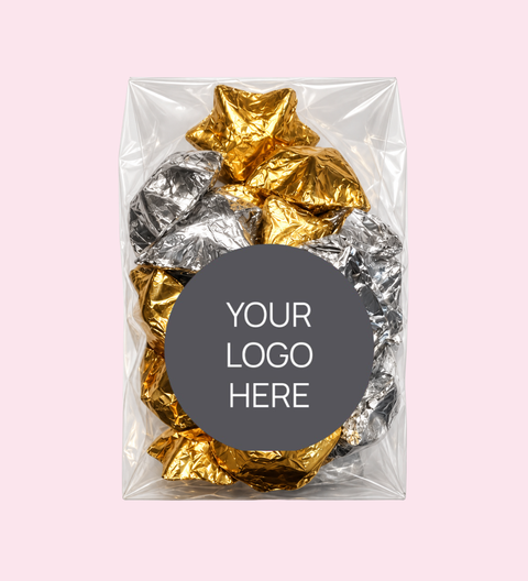 A clear plastic bag containing crumpled metallic gold and silver foil pieces, centered on a pale pink background with a dark gray circular label that reads 'YOUR LOGO HERE'.