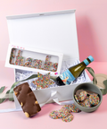 Gift box with chocolate bars, freckles, and a bottle of wine on a pink background