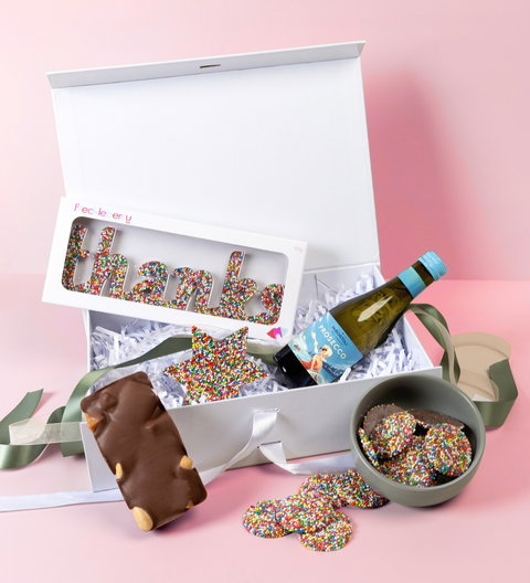 Gift box with chocolate bars, freckles, and a bottle of wine on a pink background