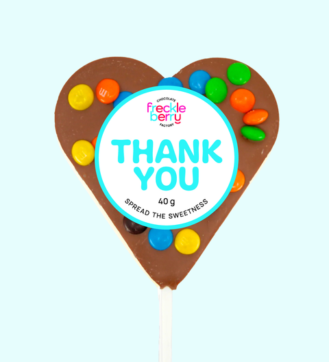 Heart-shaped chocolate lollipop with colorful candies and 'Freckle Berry' branding on a light blue background.