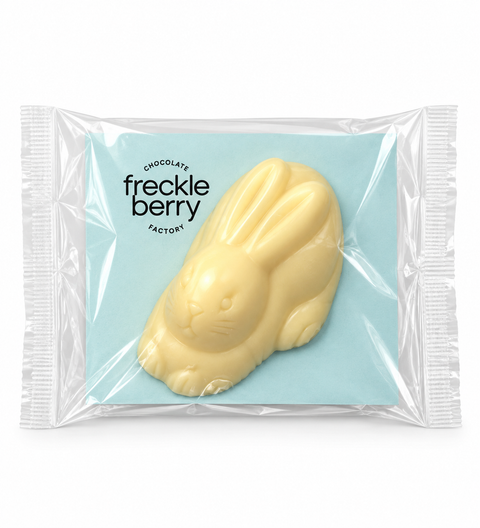 A packaged Freckle Berry chocolate bunny in pale yellow, sealed in a clear plastic bag with a light blue backing card. The brand name 'freckle berry FACTORY' is printed on the card.