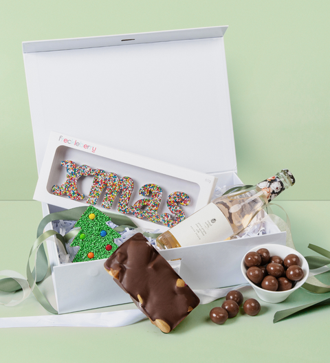 Christmas Gift box with assorted treats including a bottle, candy, and chocolate bar on a light green background.