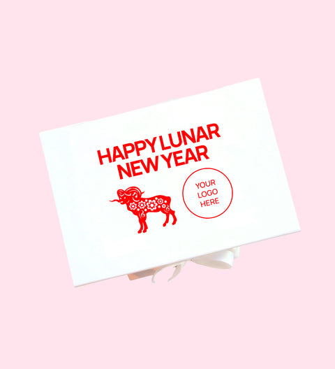 A white rectangular gift box or card package shown at an angle on a light pink background. The front has red text reading 'HAPPY LUNAR NEW YEAR,' a red ram illustration with floral patterning, and a red circular placeholder that says 'YOUR LOGO HERE.