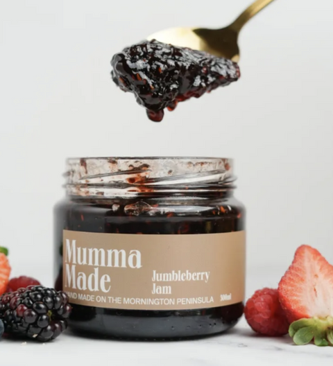 Jar of 'Mumma Made' jumbleberry jam with a spoonful above, surrounded by berries on a light background