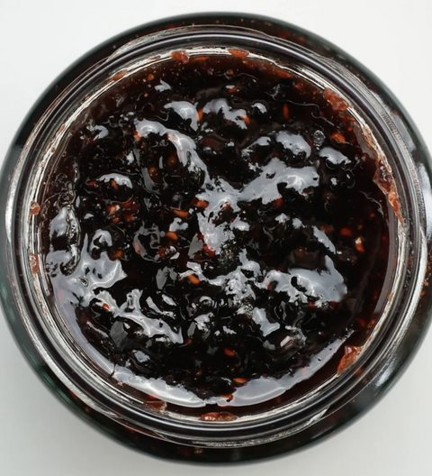 Close-up of a jar of dark jam on a white background
