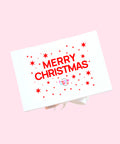 A white gift box with a 'MERRY CHRISTMAS text in multicolor and a small logo below the text.